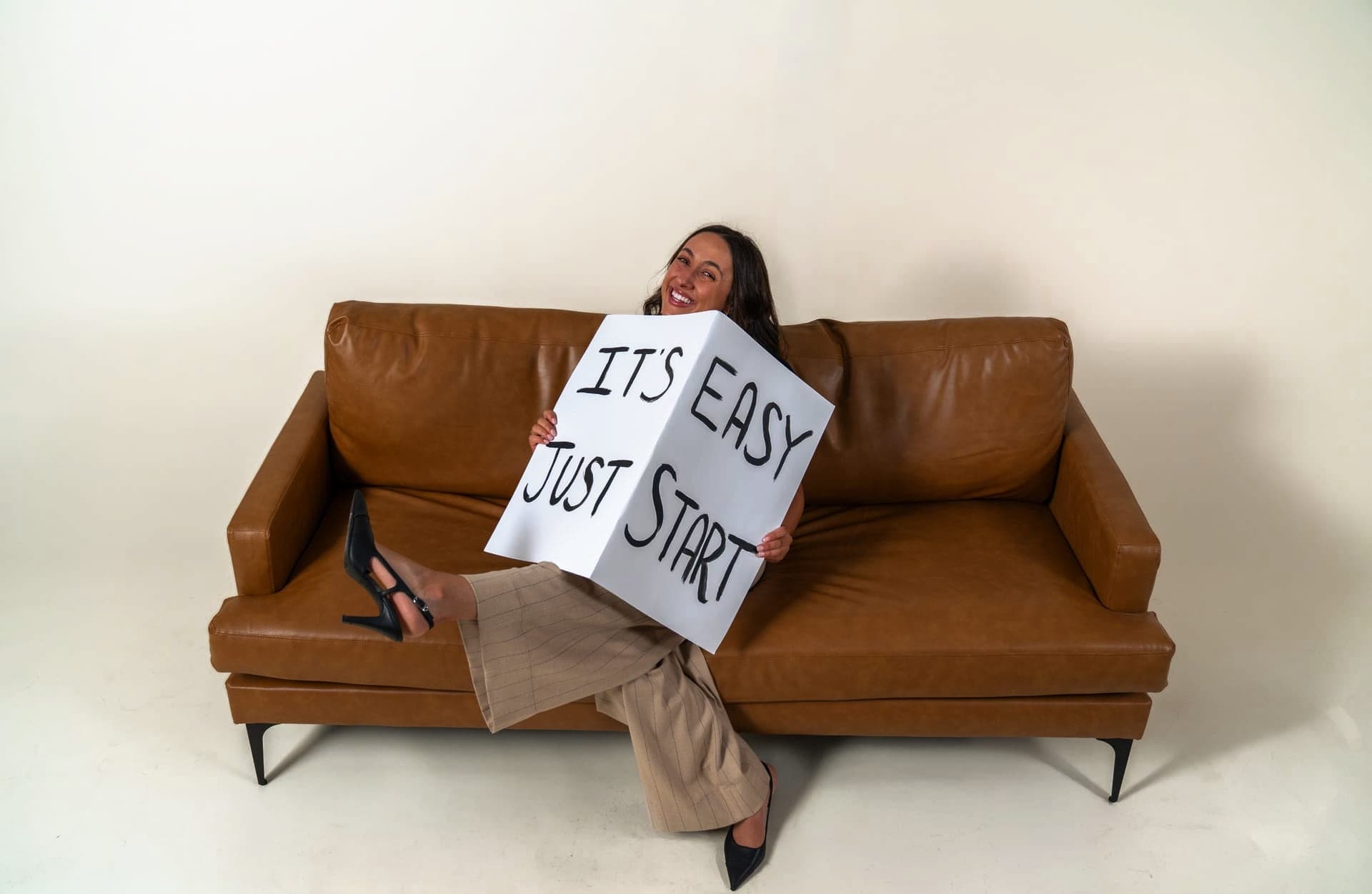 A Just Start LA coach on a couch holding a sign that reads It's Easy. Just Start.